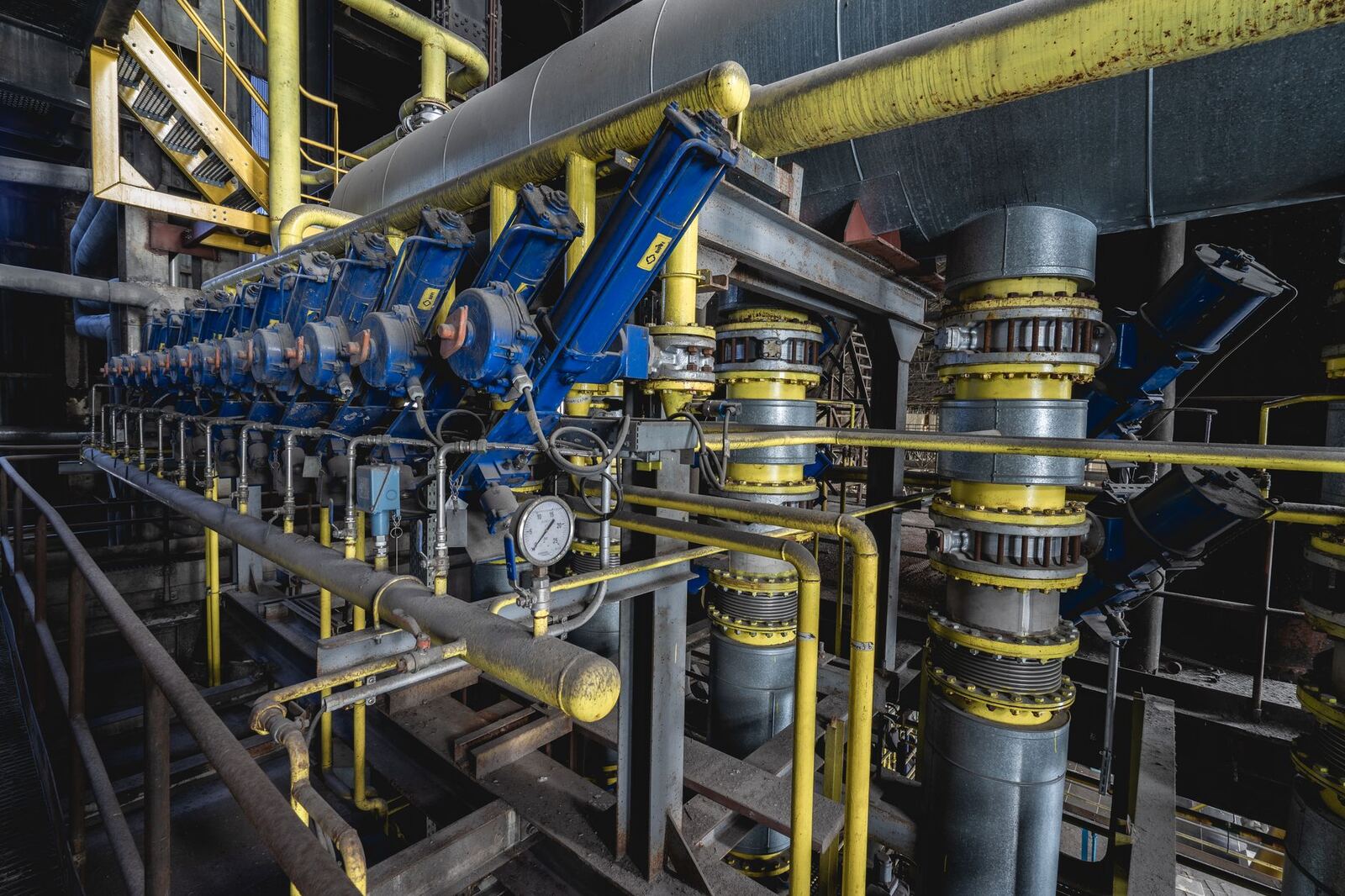 A detailed view of an industrial machine room featuring complex blue and yellow equipment and piping.