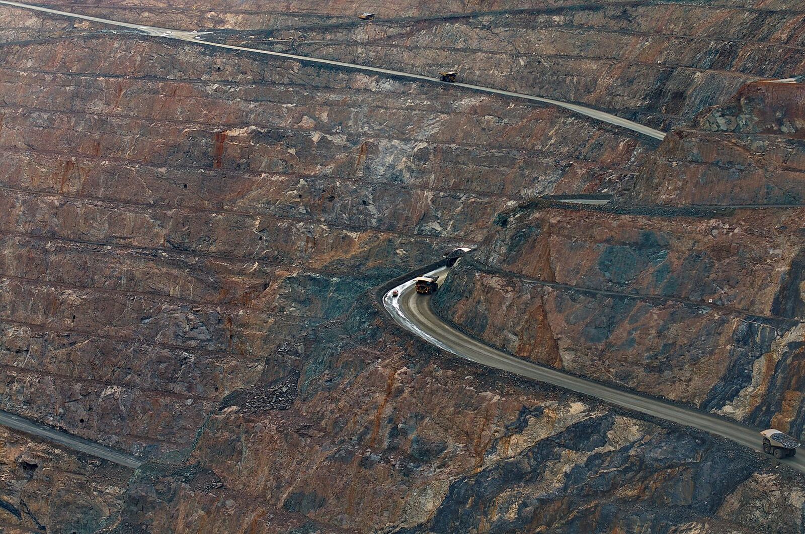 Aerial view of open-pit mine with haul trucks navigating winding roads.