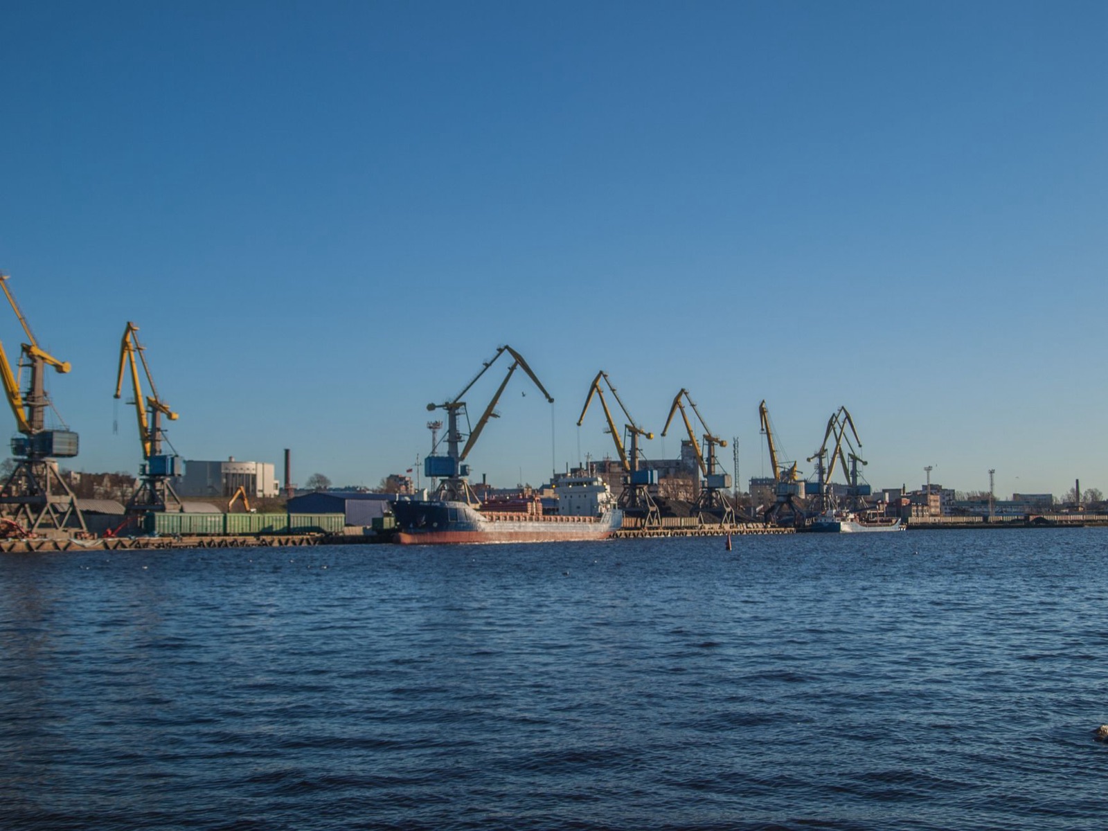 View of a bustling shipyard with cranes and ships under a clear blue sky.
