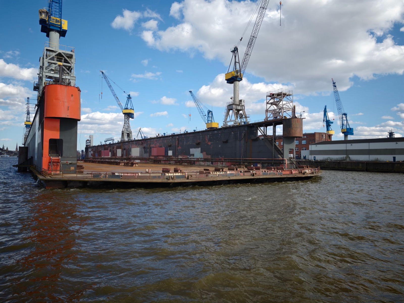 A shipyard featuring a docked vessel and multiple cranes under a bright blue sky.