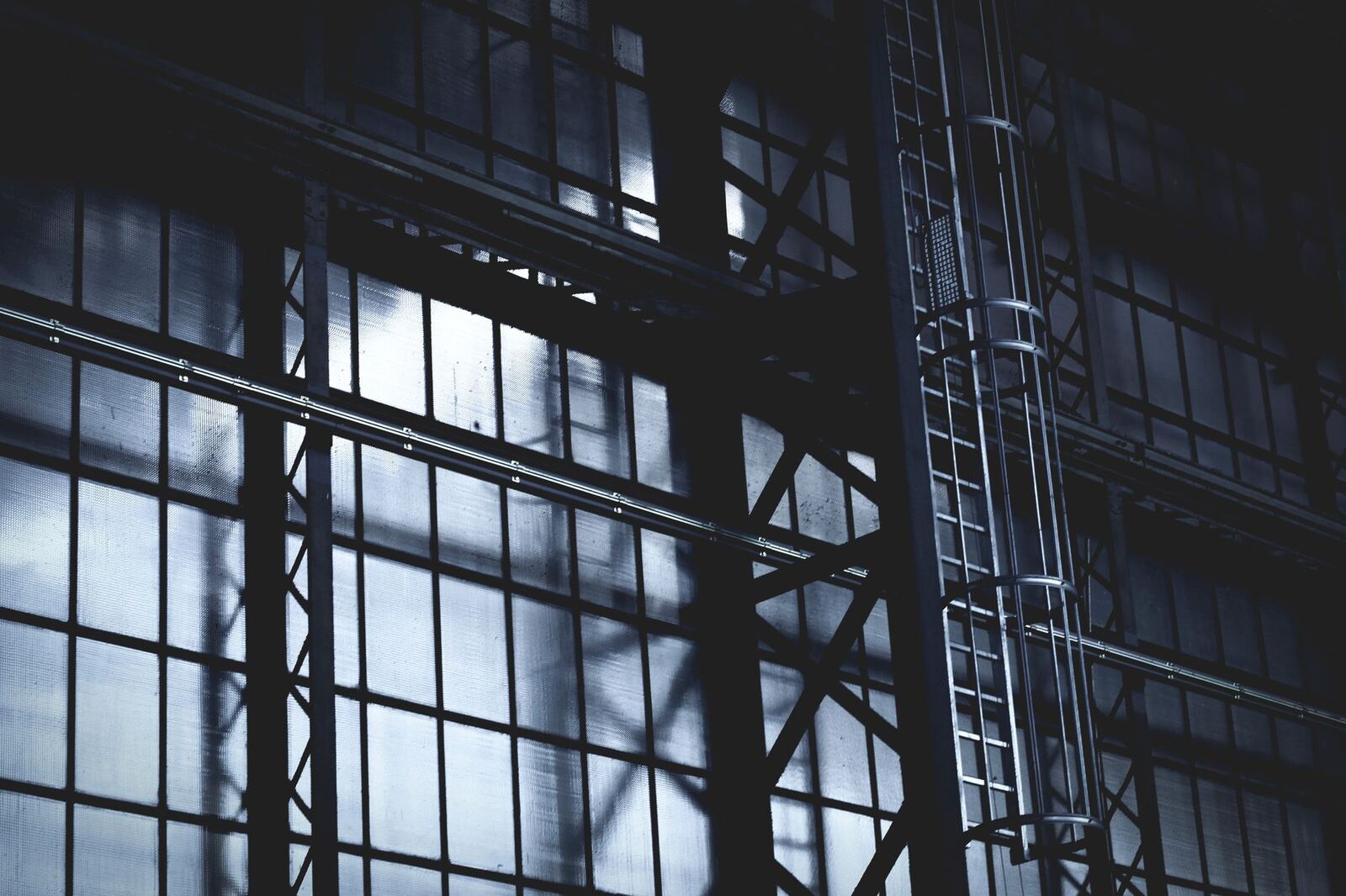 Dramatic view of a steel frame and ladder in an industrial setting with sunlight casting shadows.