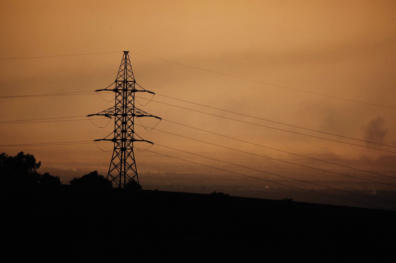 A power transmission tower silhouette against a warm sunset sky, symbolizing energy and infrastructure.